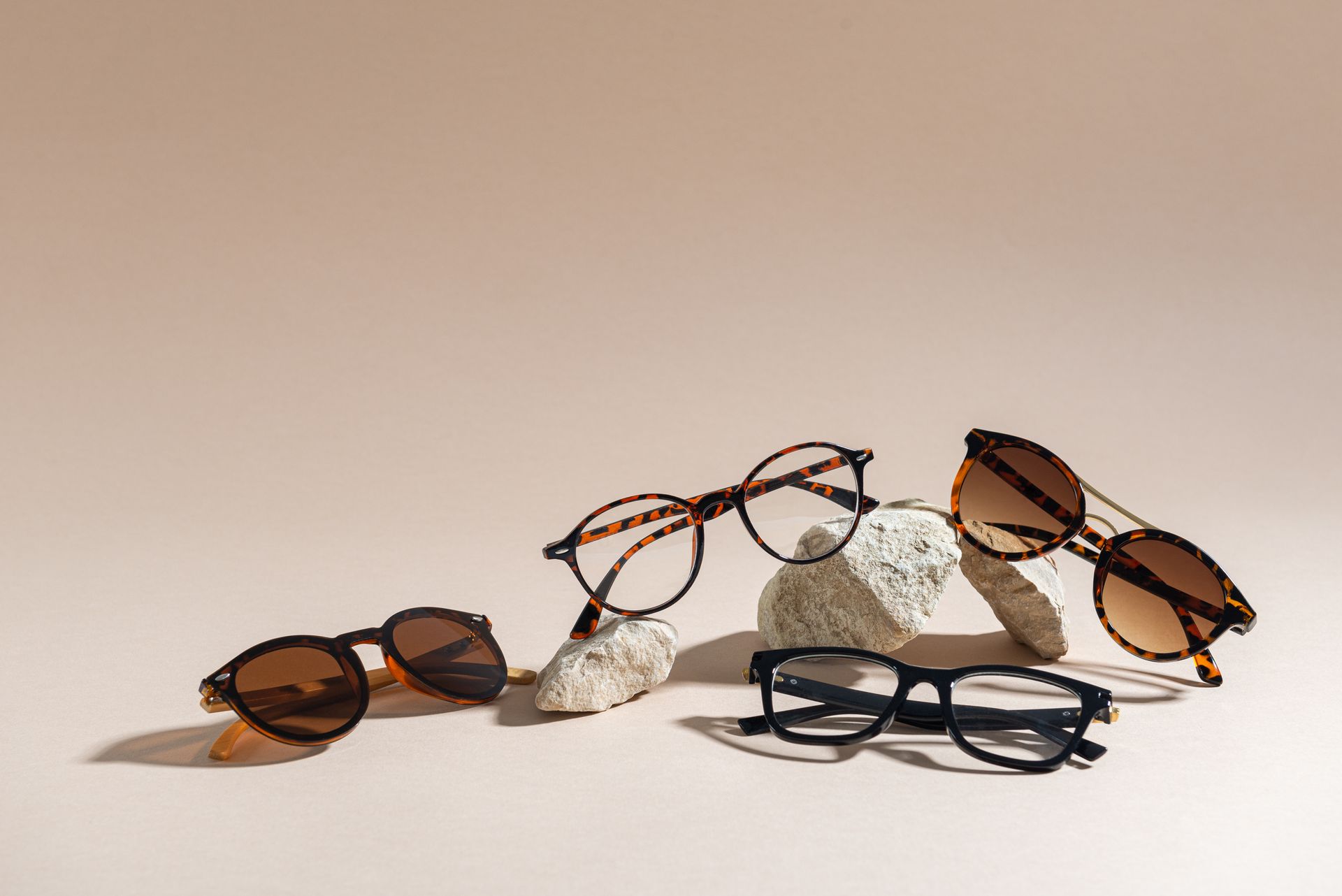 Cinq paires de lunettes, à montures rondes et rectangulaires, sont posées sur des pierres sur un fond rose.