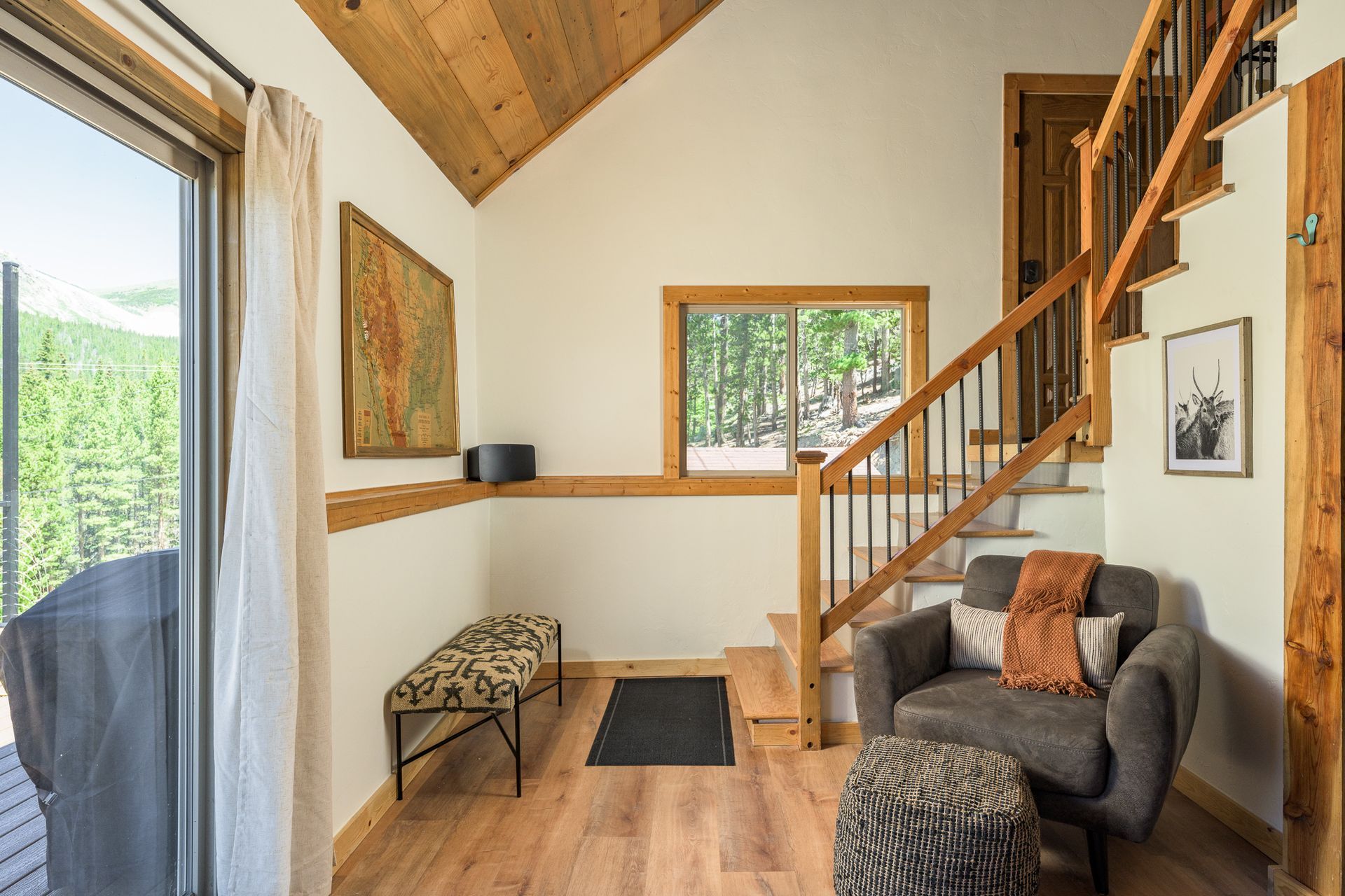 Cozy interior with wood accents: Entryway with stairs, armchair, bench, artwork, and a sliding glass door to a green view.