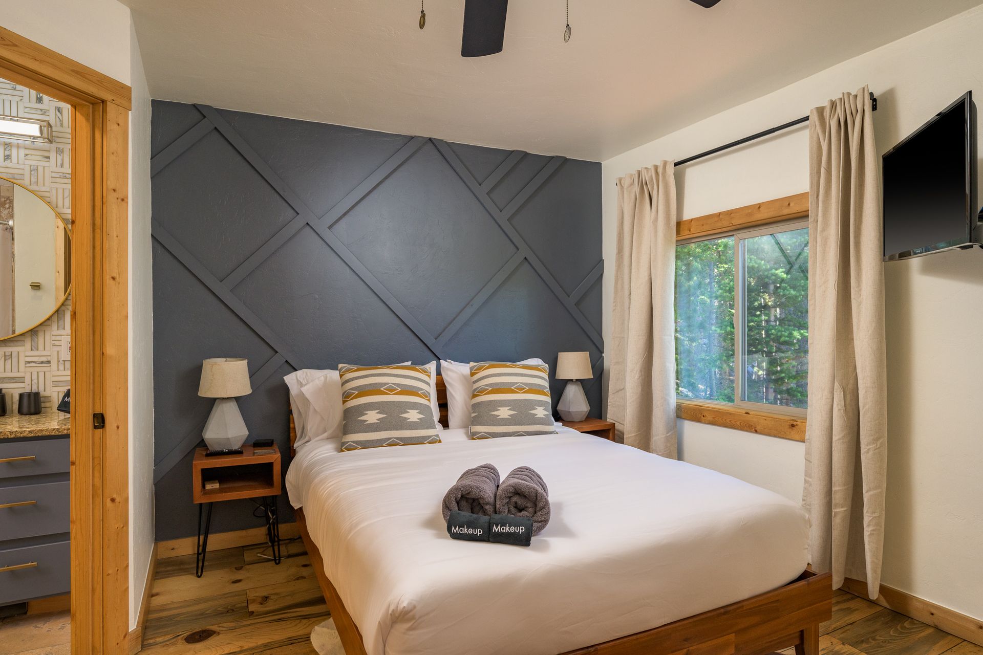 Bedroom with a wooden bed, gray accent wall, small lamps, and a view to outside.