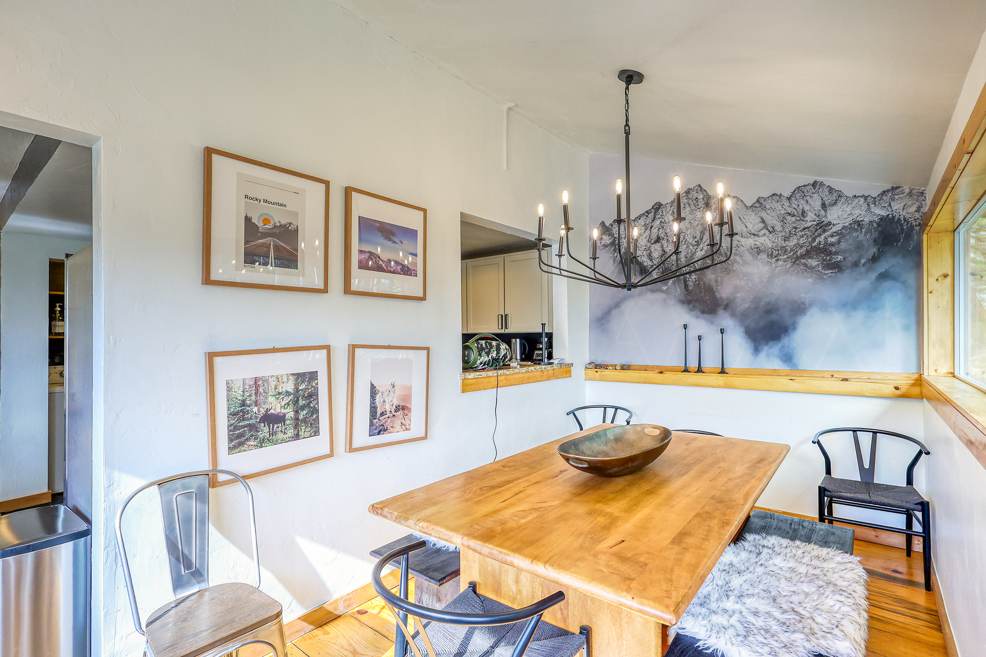 Dining room with wood table, black chairs, mountain mural, artwork, and a chandelier.