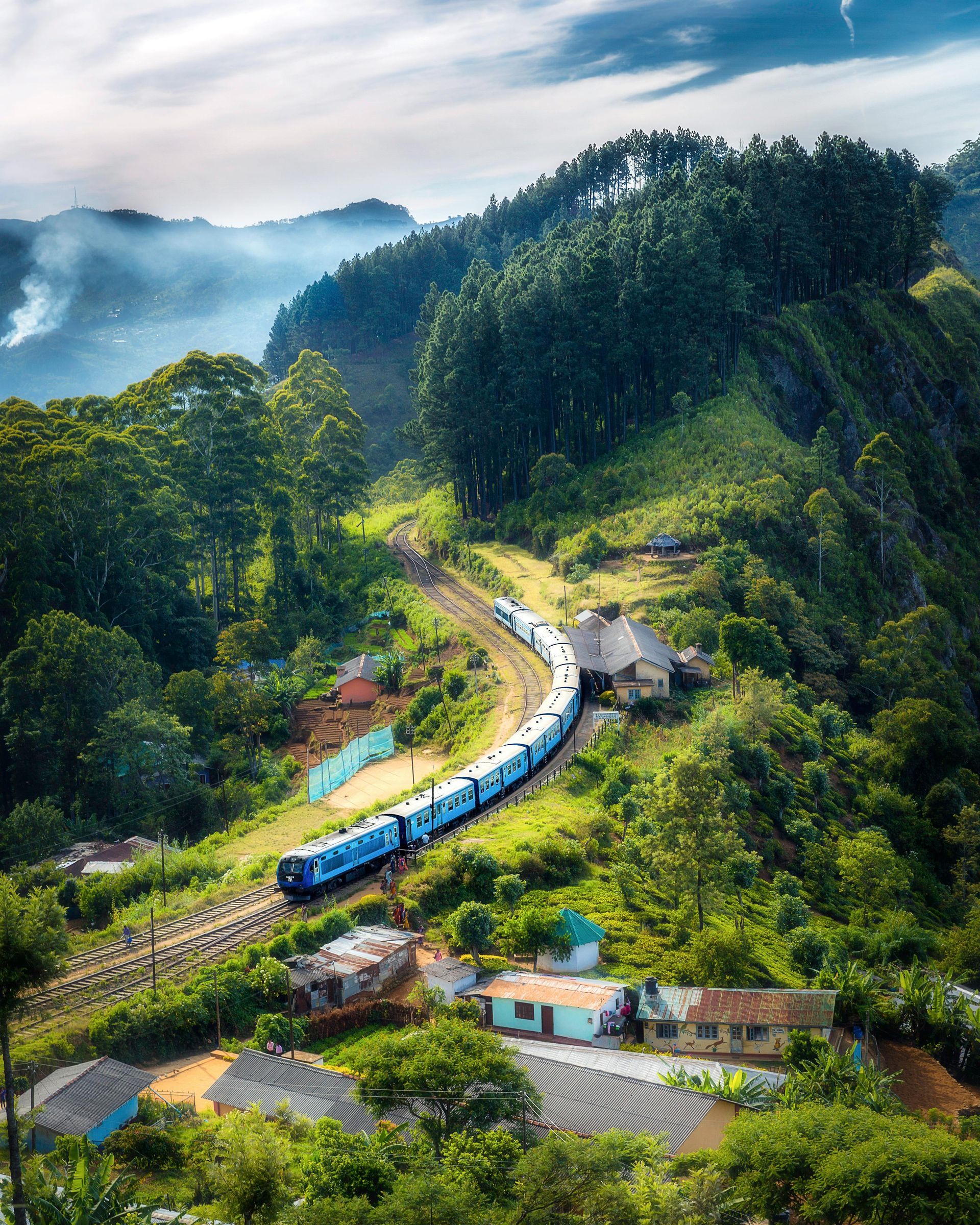 Train winding through lush green hills and houses, Sri Lanka.