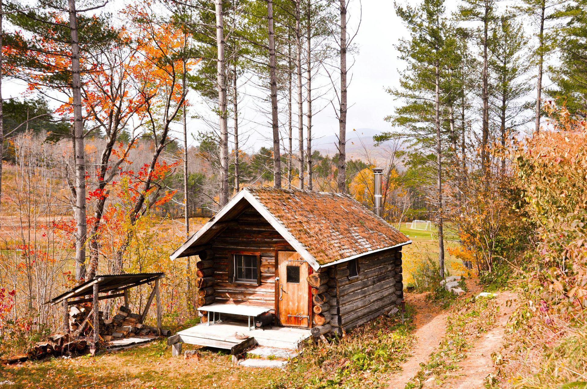 Wooden cabin in autumn woods, with orange and yellow foliage.