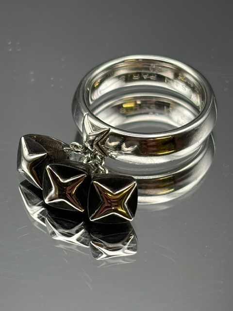 Gros plan de mains tenant une bague avec une pince à épiler sur un établi, avec des lumières floues en arrière-plan.