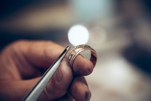 Gros plan de mains tenant une bague avec une pince à épiler sur un établi, avec des lumières floues en arrière-plan.
