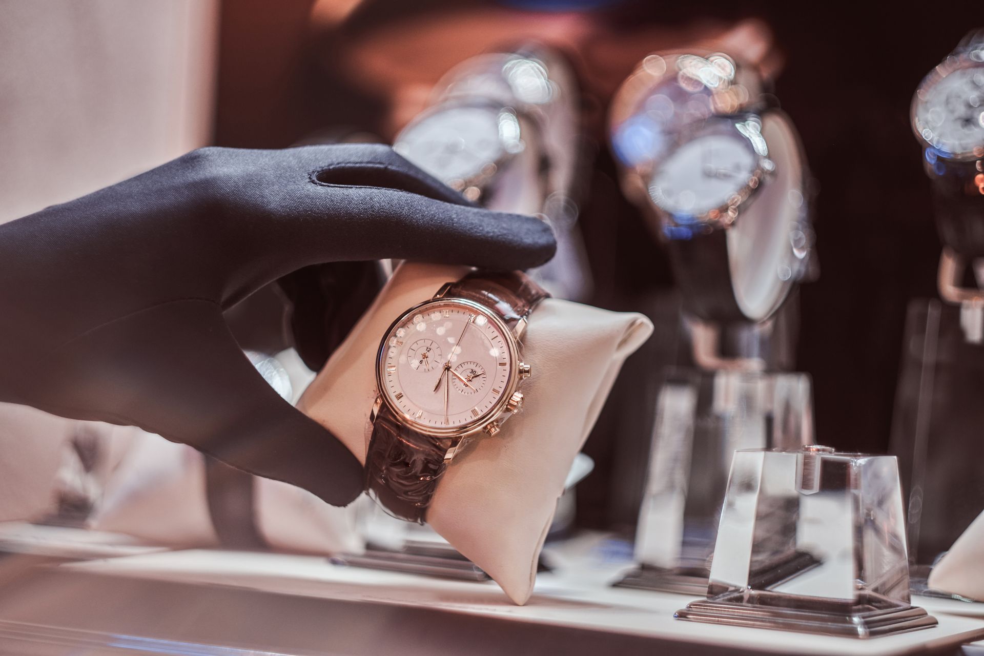 Main gantée tenant une montre-bracelet en or sur un coussin de présentation dans une bijouterie