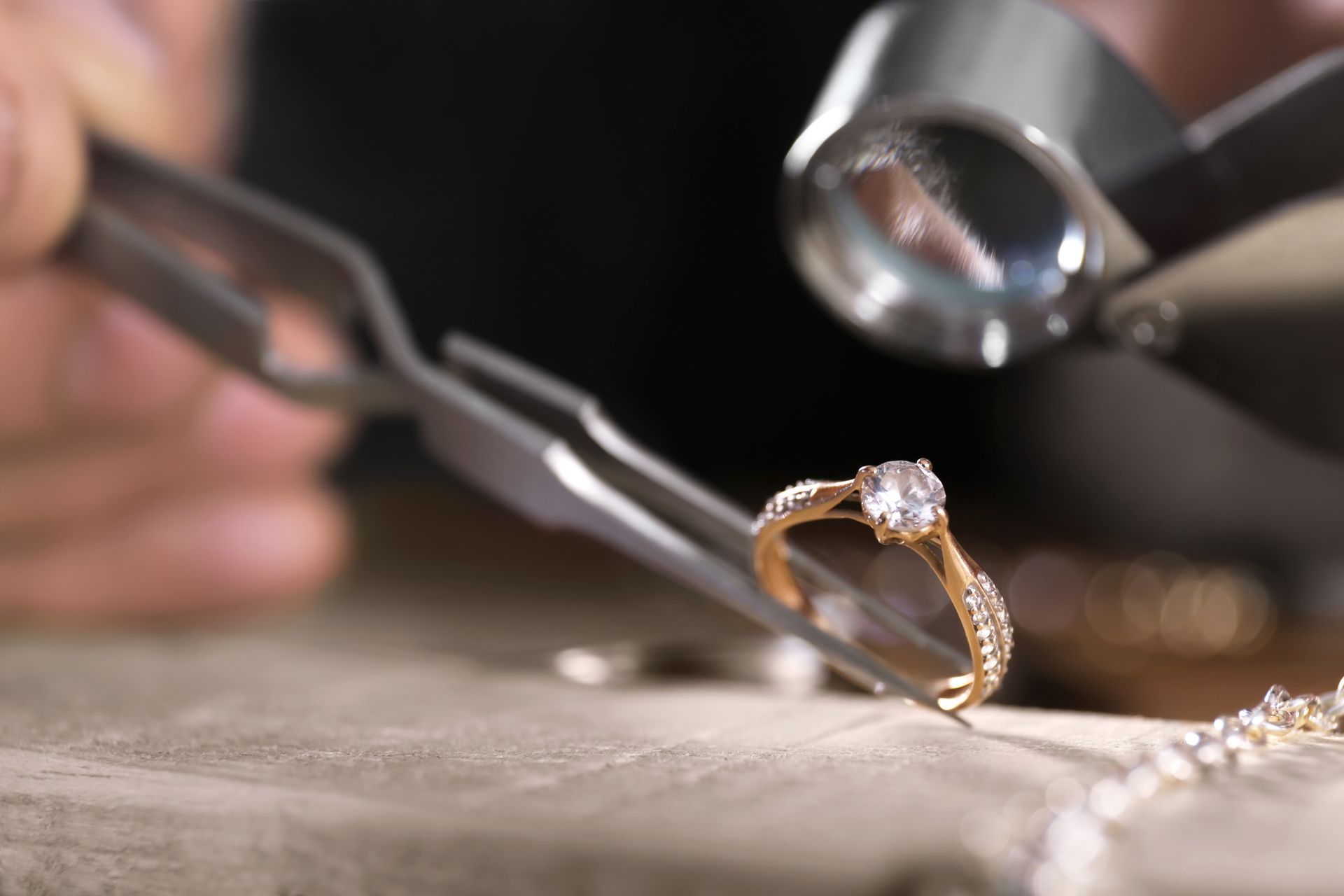 Gros plan sur une bague de fiançailles en or examinée à la loupe d'un bijoutier sur un établi.