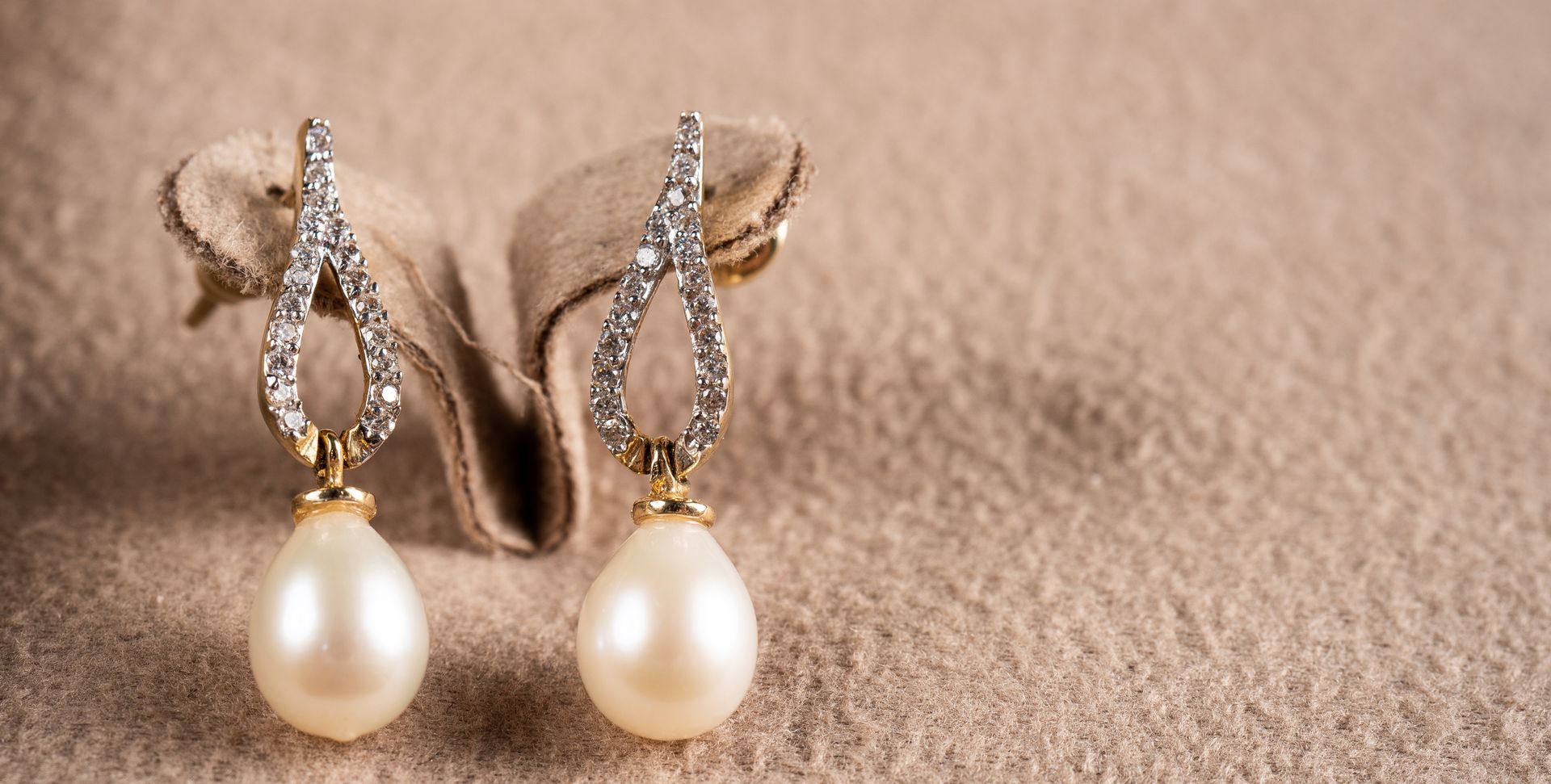Boucles d'oreilles pendantes en perles avec détails argentés et dorés sur fond de tissu beige