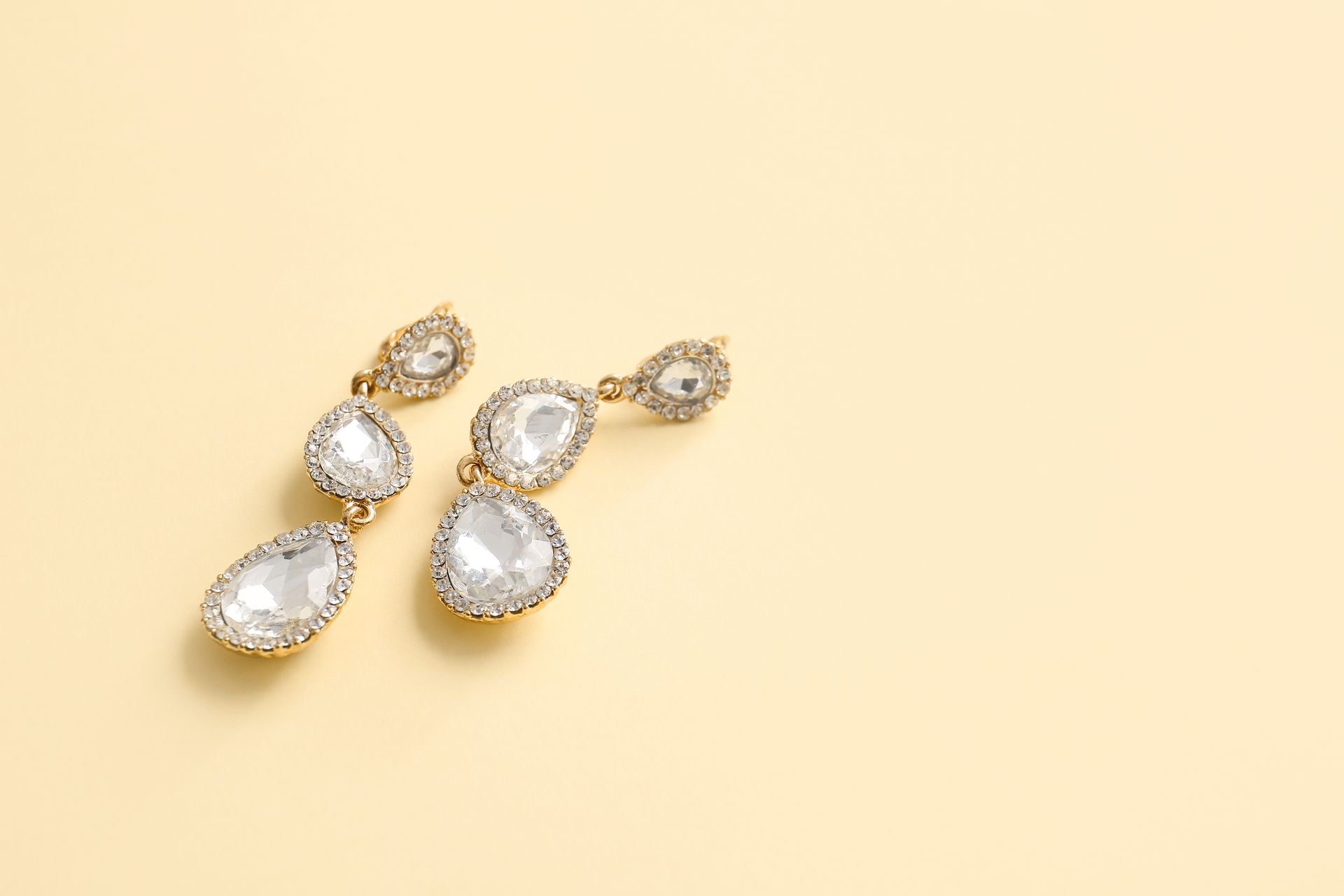 Boucles d'oreilles pendantes en or et cristal transparent sur fond beige