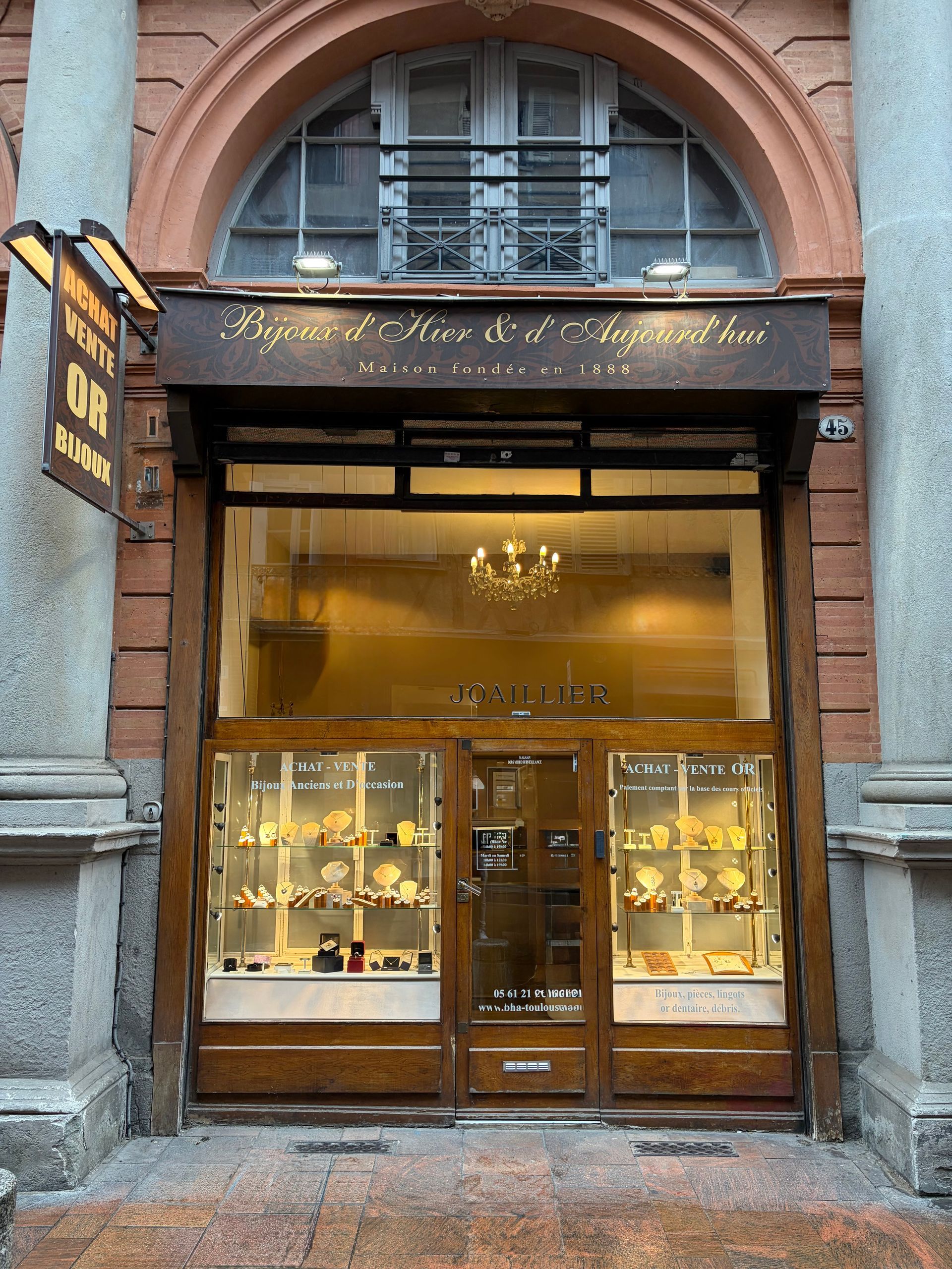 Entrée de magasin avec de grandes fenêtres cintrées et des vitrines dans un bâtiment en briques.