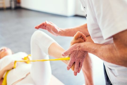 Therapeut hilft einem Patienten in einer Klinik, sein Bein mit einem gelben Band zu strecken.