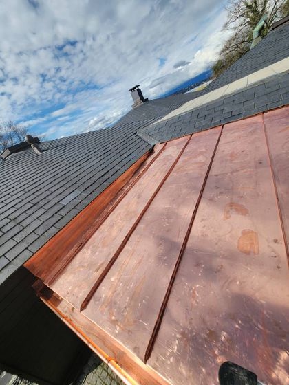Partie de toit en bois avec bardeaux gris et cheminée sous un ciel nuageux
