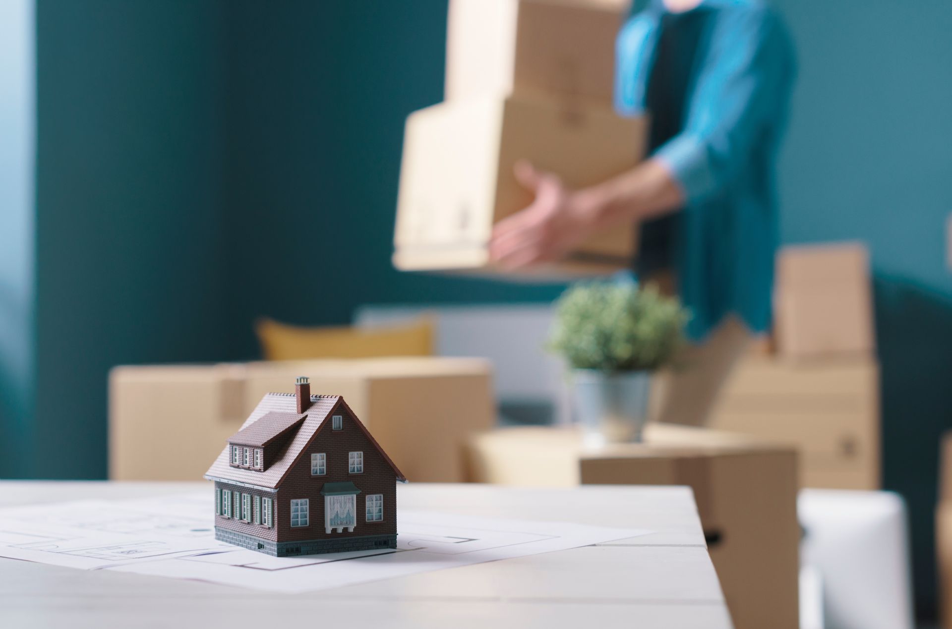 Une petite maison en premier plan et un homme qui porte des cartons
