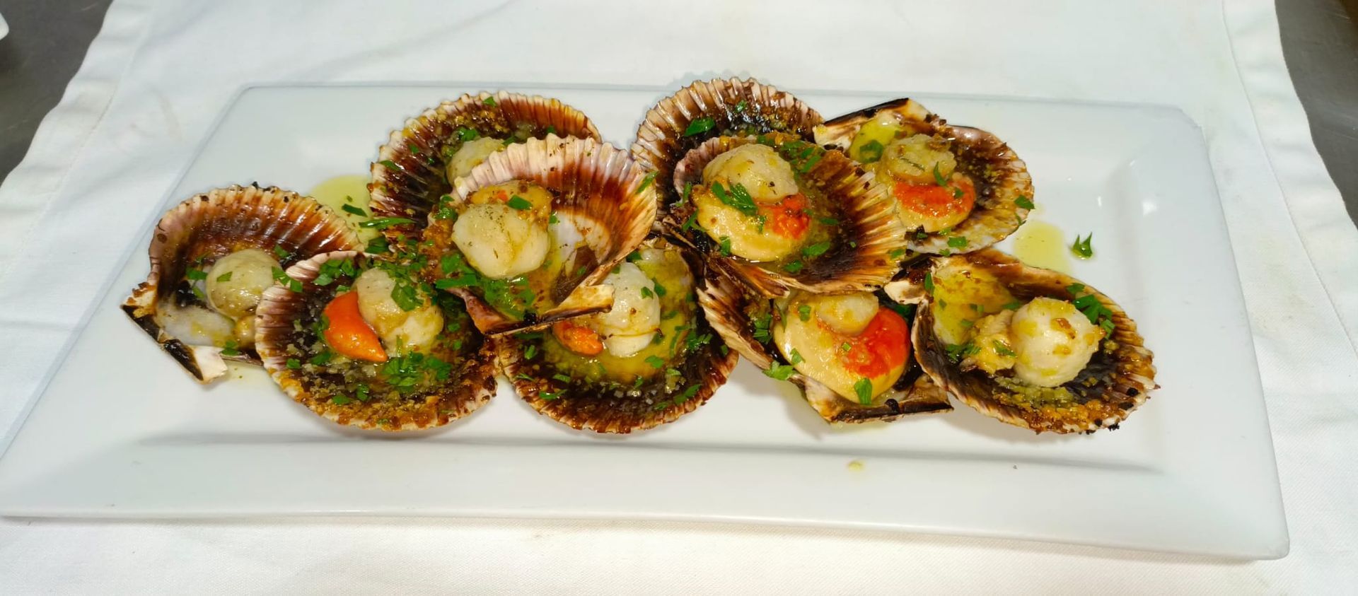 Vieiras a la parrilla servidas en sus conchas en un plato rectangular blanco.