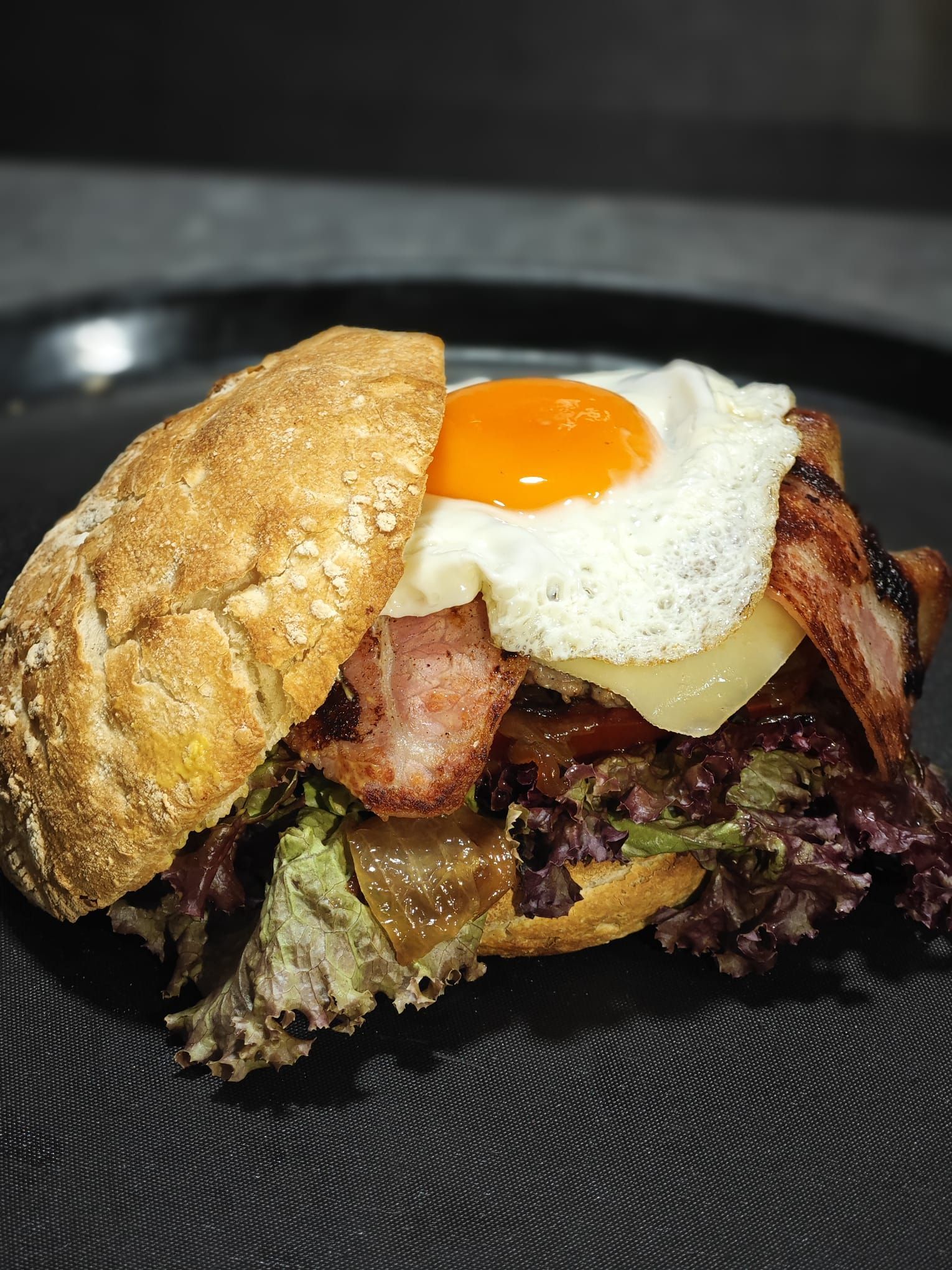 Sándwich con huevo frito, tocino, queso y lechuga en un pan.