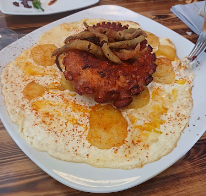 Plato de comida a base de pulpo, patatas y salsa cremosa.