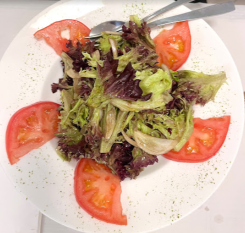 Ensalada con lechuga, cebolla y rodajas de tomate en un plato blanco con cubiertos.