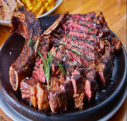 Filete de ternera cortado a la parrilla sobre un plato negro, adornado con romero y sal.