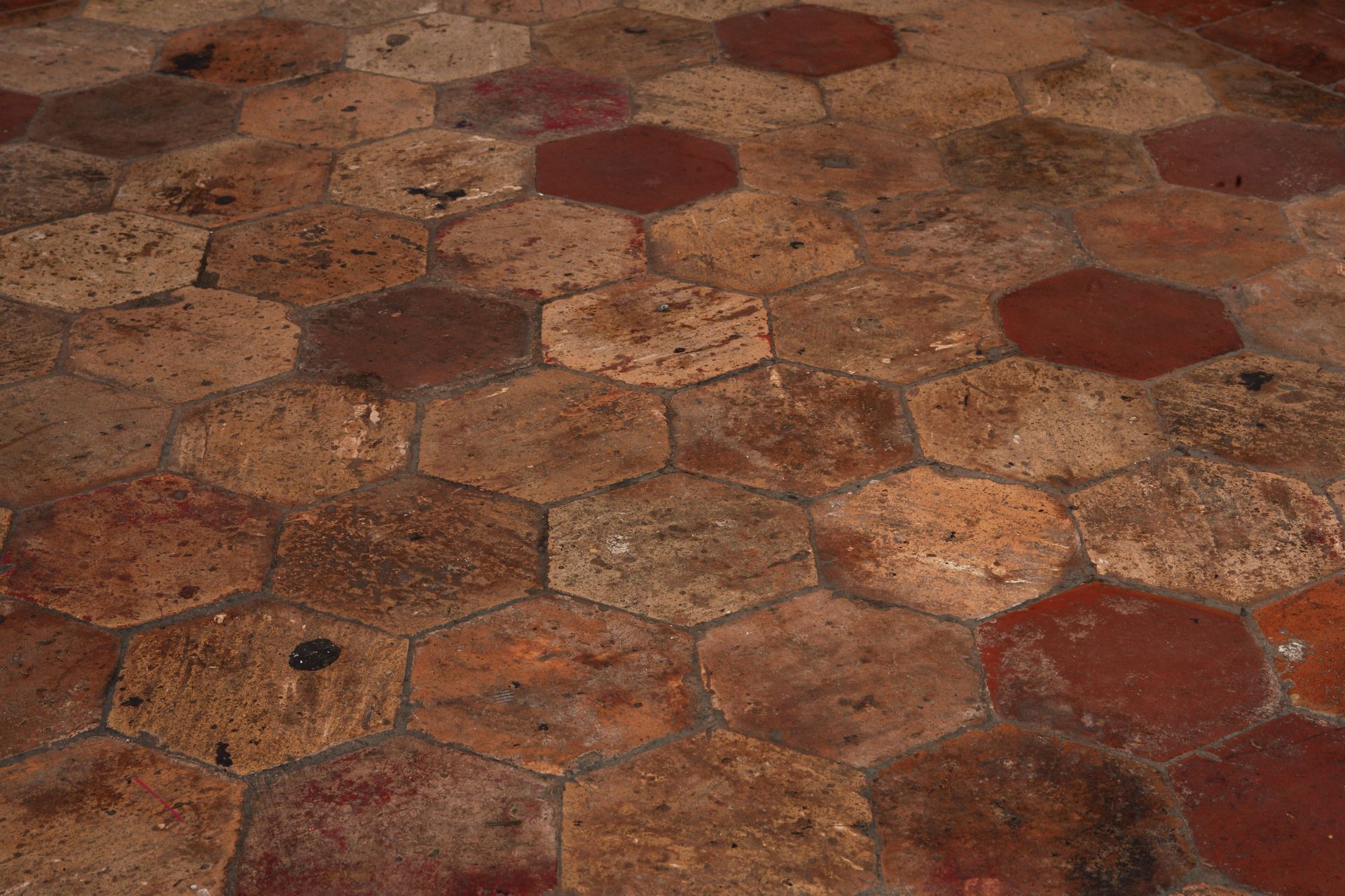 Des carreaux de pierre hexagonaux patinés, dans des tons de rouge et de brun terreux, forment une surface de sol texturée.