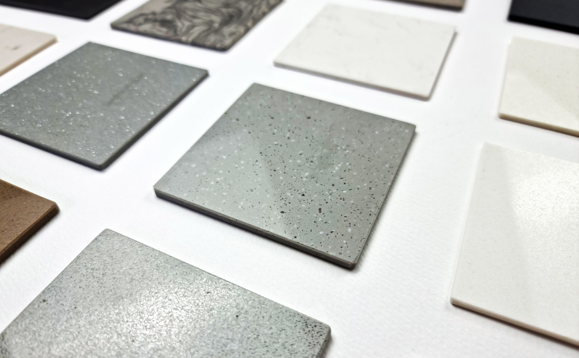 Échantillons de peinture carrés assortis, gris, blancs et beiges, disposés sur une surface blanche.