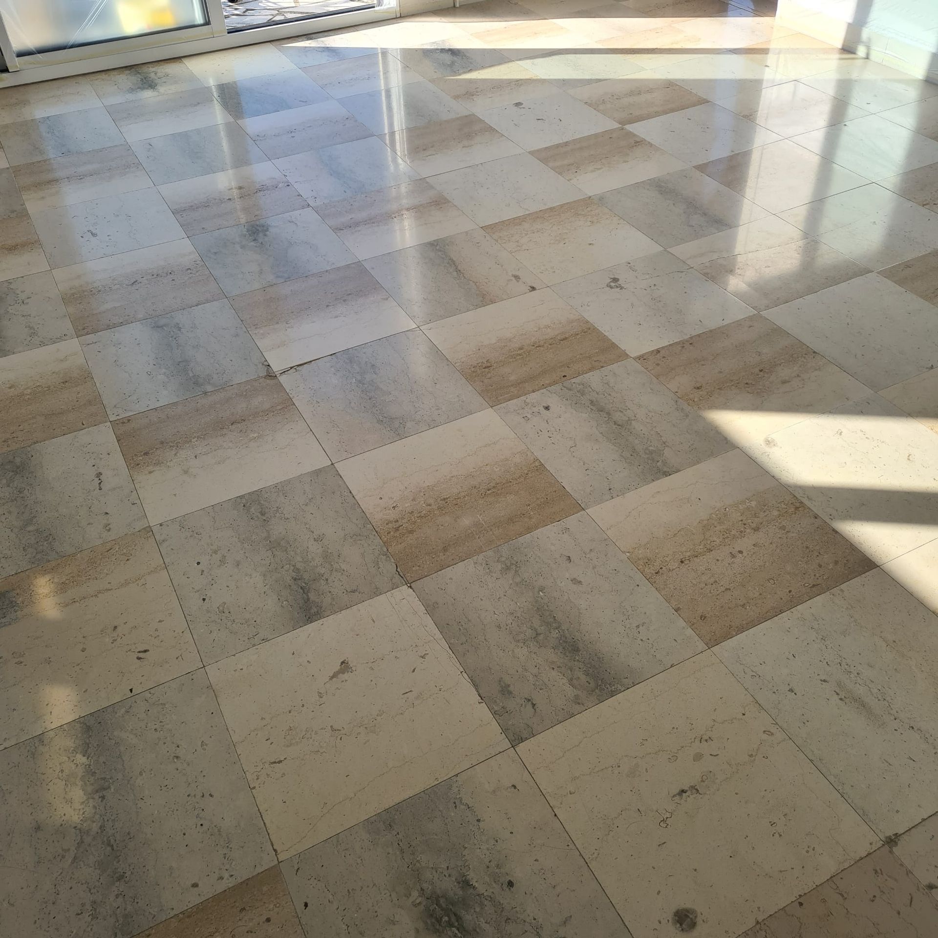 Sol carrelé beige baigné de soleil, avec reflets de fenêtres et ombres diagonales.