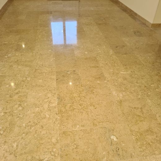 Le sol du couloir en marbre beige poli reflète une fenêtre située au fond.