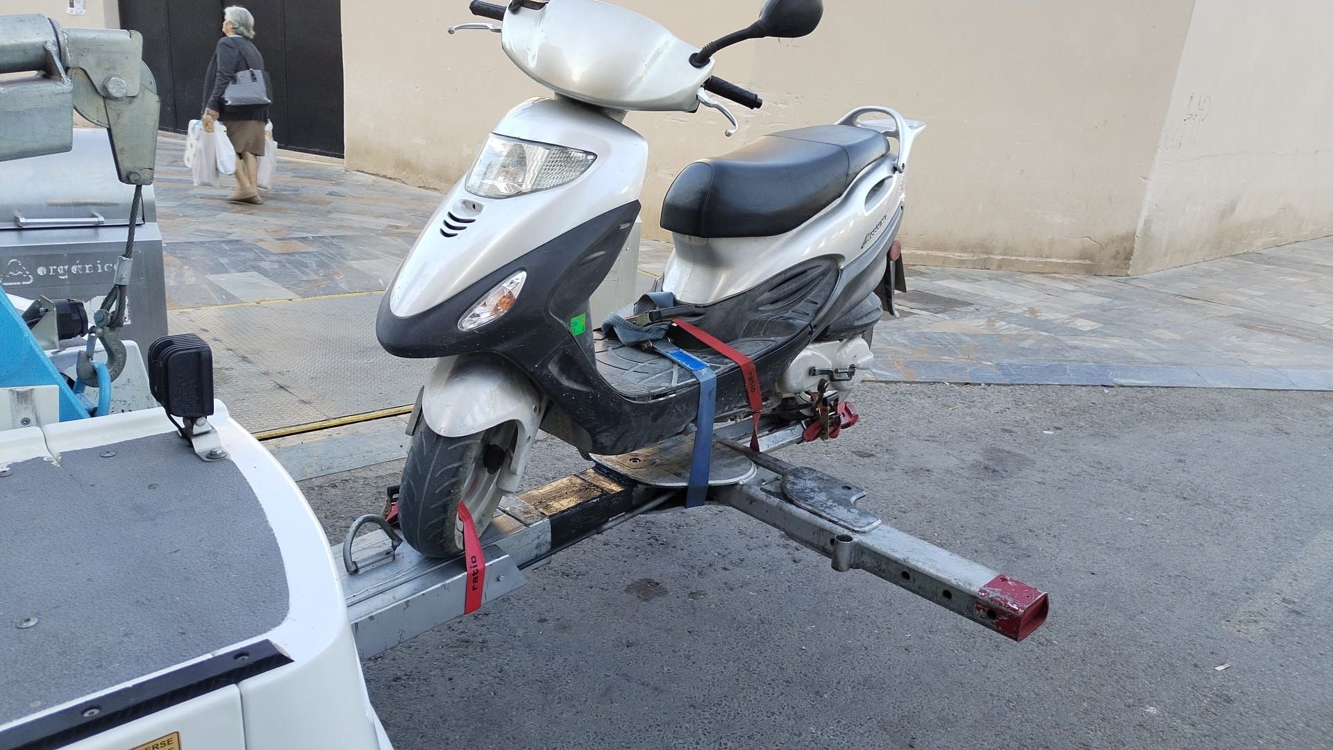 Scooter plateado remolcado en un remolque por una calle de la ciudad.