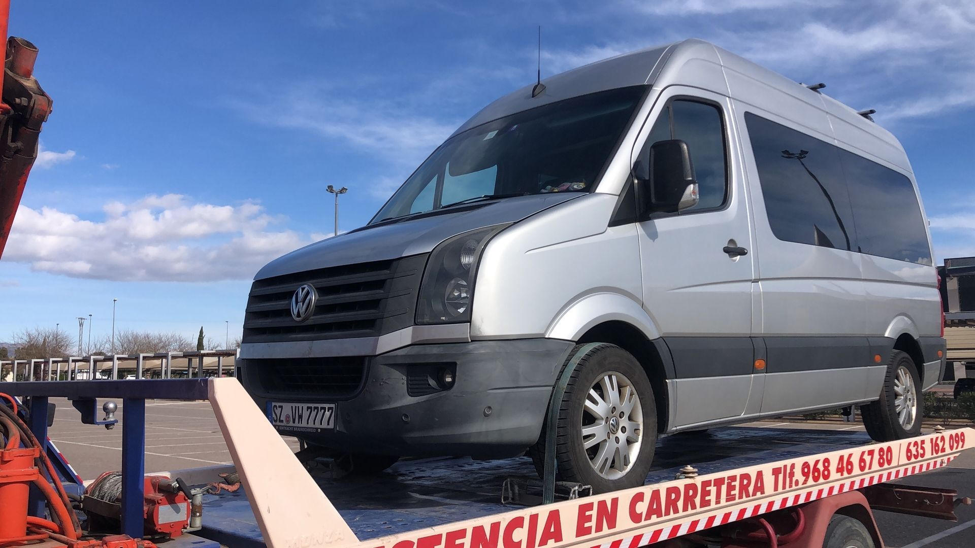 Furgoneta plateada remolcada en una plataforma de camión en un día soleado.