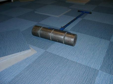 Um eine gute Haftung zum Unterboden zu erzielen werden die Teppichfliesen mit schweren Eisenrollen angewalzt.
