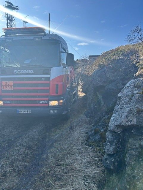 Punainen Scania-kuorma-auto jumissa kivisen tienvarren vieressä aurinkoisena päivänä