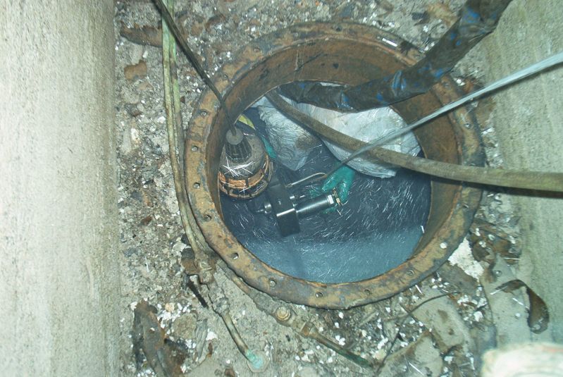 Avoin lattiakaivo, jossa on sameaa vettä, putkia ja kaapeleita karkeassa betonireiässä