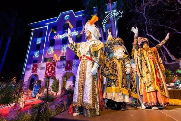 Artistas disfrazados en un colorido escenario iluminado, luciendo elaborados trajes dorados y naranjas por la noche.