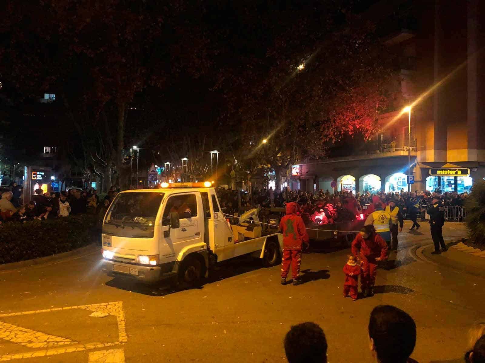 Grúa de remolque y personal de emergencia con equipo rojo en una escena nocturna en la calle con transeúntes.