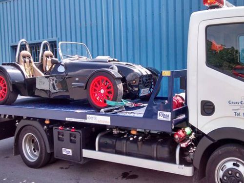 Una grúa transporta un coche de carreras descapotable negro con ruedas de color rojo brillante sobre una plataforma.