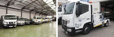 Camiones blancos estacionados dentro de un almacén, incluyendo una grúa en primer plano.