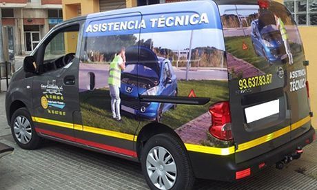 Furgoneta negra de asistencia con la inscripción “ASISTÊNCIA TÉCNICA” estacionada en una calle mojada.