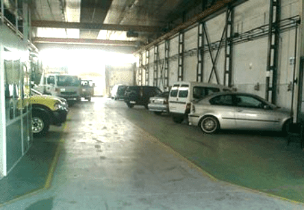 Almacén interior con varios coches aparcados y una entrada luminosa y diáfana.