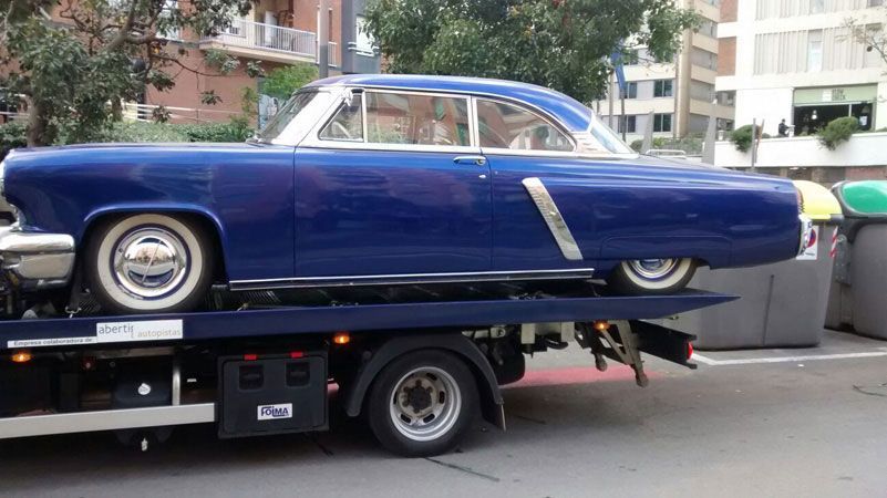 Un coche clásico azul subido a una grúa en una calle de la ciudad.