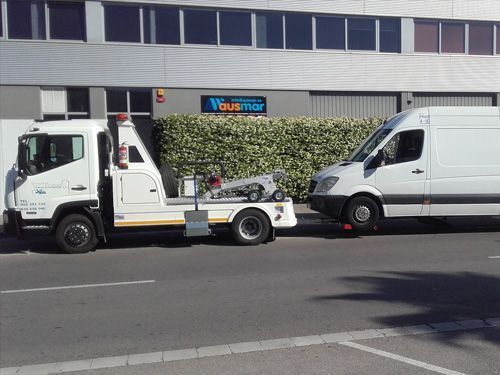 Una grúa blanca remolca una furgoneta blanca en una calle de la ciudad, frente a un edificio.