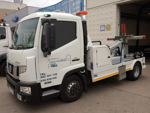 Camioneta blanca de servicio público estacionada junto a un edificio, con equipo montado en la parte trasera.