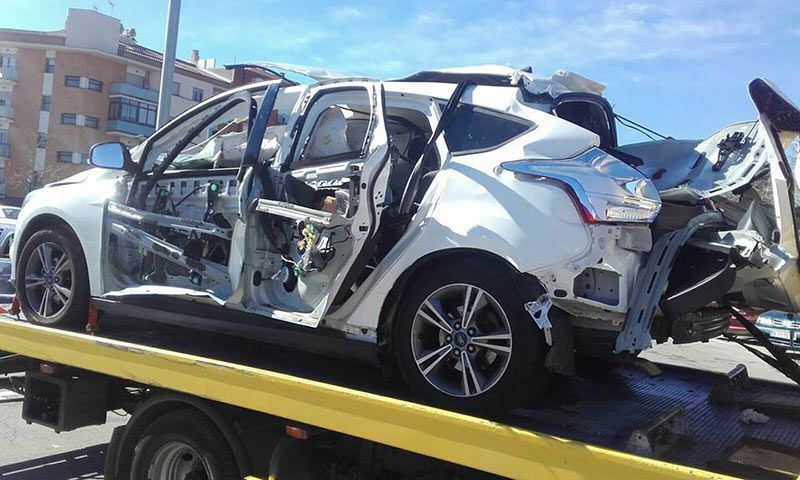 Un SUV blanco gravemente dañado, sobre una grúa, con los laterales abollados y las puertas abiertas tras un accidente.