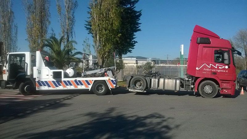 Un camión semirremolque rojo con una plataforma blanca estacionado en una calle soleada.