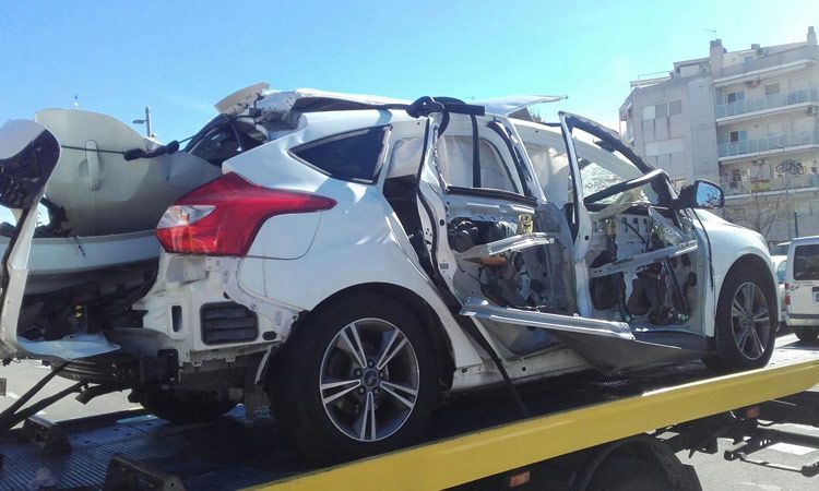Un SUV blanco gravemente dañado, remolcado por una grúa tras una colisión, presenta las puertas abolladas y daños en la parte trasera.