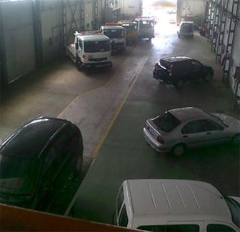 Varios coches y furgonetas estaban aparcados dentro de un gran garaje con aspecto de almacén, y un coche giraba cerca del centro.