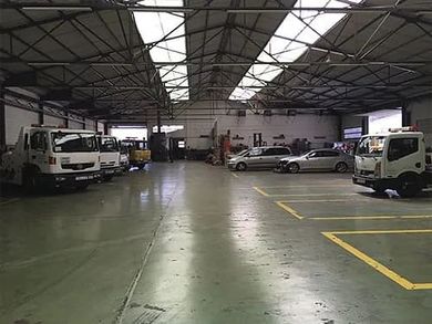 Amplio garaje para vehículos con camiones, coches y furgonetas aparcados bajo un alto techo metálico.