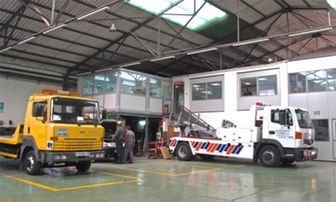 Dos camiones de servicios públicos, uno amarillo y otro blanco, estaban estacionados dentro de un almacén, con trabajadores cerca.