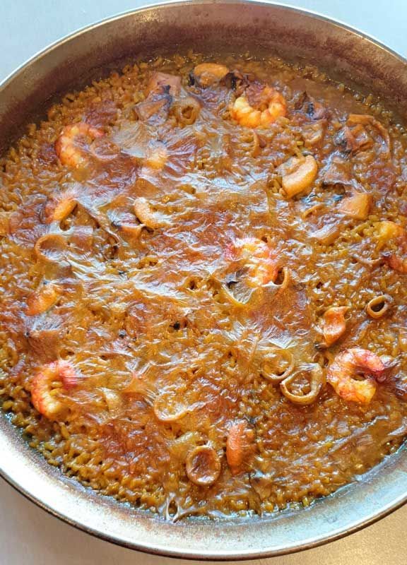 Una sartén llena de arroz y camarones está sobre una mesa.