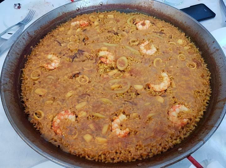 Una sartén de paella con camarones y verduras sobre una mesa.