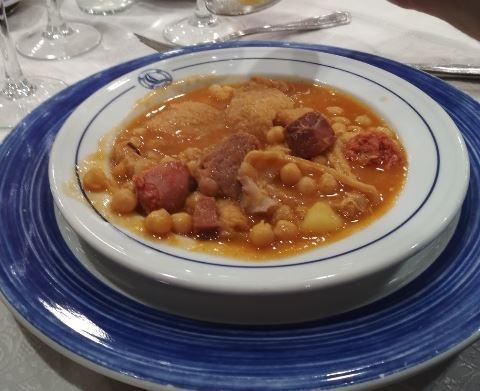 Un tazón de sopa con garbanzos y carne en un plato azul.