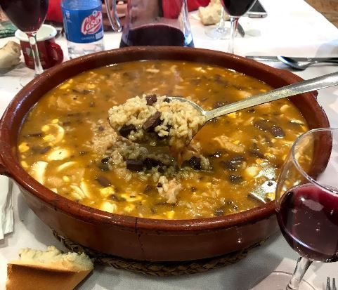 Un tazón de sopa con una cuchara y un vaso de vino.
