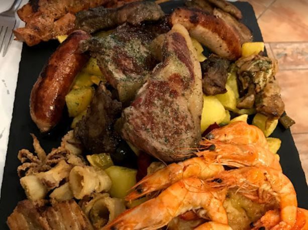 Un plato de comida con carne, camarones, patatas y salchichas en una mesa.